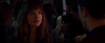 Movie still from “Fifty Shades of Grey” (2015), directed by Sam Taylor-Johnson – A woman sitting in a dark room with other people in the background; Close Up shot, Over the shoulder angle
