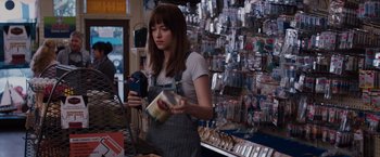 Movie still from “Fifty Shades of Grey” (2015), directed by Sam Taylor-Johnson – A woman in a store holding a can of soda; Medium shot, Over the shoulder angle