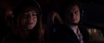 Movie still from “Fifty Shades of Grey” (2015), directed by Sam Taylor-Johnson – A man and a woman with headphones in a dark room; Close Up shot, Over the shoulder angle