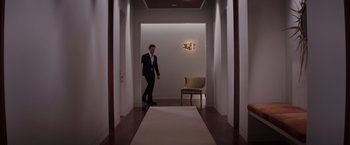 Movie still from “Fifty Shades of Grey” (2015), directed by Sam Taylor-Johnson – A man standing in a hallway next to a chair; Wide shot, High angle
