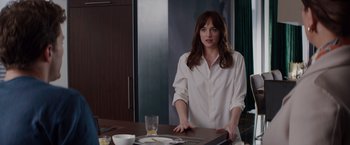 Movie still from “Fifty Shades of Grey” (2015), directed by Sam Taylor-Johnson – A woman standing at a table in a kitchen; Medium shot, Over the shoulder angle