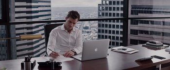 Movie still from “Fifty Shades of Grey” (2015), directed by Sam Taylor-Johnson – A man sitting in front of an open laptop computer on top of a desk; Medium shot, High angle