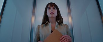 Movie still from “Fifty Shades of Grey” (2015), directed by Sam Taylor-Johnson – A woman holding an envelope while standing in an escalator; Close Up shot, Low angle