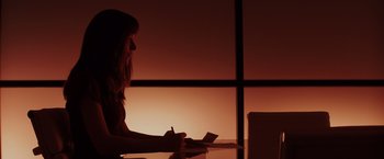 Movie still from “Fifty Shades of Grey” (2015), directed by Sam Taylor-Johnson – A woman sitting at a table writing on a piece of paper; Medium shot, Over the shoulder angle