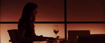 Movie still from “Fifty Shades of Grey” (2015), directed by Sam Taylor-Johnson – A woman sitting at a table with a glass of red wine; Medium shot, Over the shoulder angle