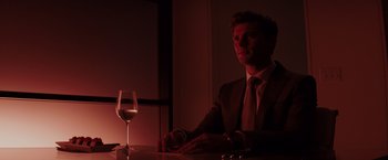 Movie still from “Fifty Shades of Grey” (2015), directed by Sam Taylor-Johnson – A man sitting at a table with a glass of wine; Medium shot, Over the shoulder angle