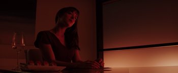 Movie still from “Fifty Shades of Grey” (2015), directed by Sam Taylor-Johnson – A woman sitting at a table in a dimly - lit room; Medium shot, Low angle