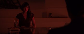 Movie still from “Fifty Shades of Grey” (2015), directed by Sam Taylor-Johnson – A woman sitting at a table in a dark room; Medium shot, Over the shoulder angle