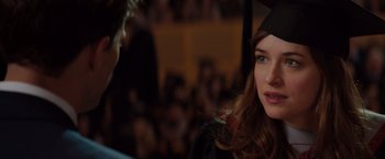 Movie still from “Fifty Shades of Grey” (2015), directed by Sam Taylor-Johnson – A woman wearing a graduation cap and gown; Close Up shot, Over the shoulder angle