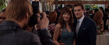 Movie still from “Fifty Shades of Grey” (2015), directed by Sam Taylor-Johnson – A man taking a picture of a woman in a blue dress; Medium shot, Over the shoulder angle