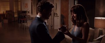 Movie still from “Fifty Shades of Grey” (2015), directed by Sam Taylor-Johnson – A man and a woman holding hands in a living room; Medium shot, Over the shoulder angle