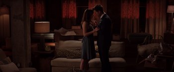 Movie still from “Fifty Shades of Grey” (2015), directed by Sam Taylor-Johnson – A man and a woman standing in front of a couch in a living room; Wide shot, High angle