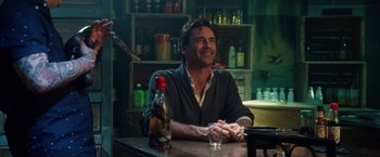Movie still from “Keeping Up with the Joneses” (2016), directed by Greg Mottola – A man sitting at a table with a bottle of wine; Medium shot, Over the shoulder angle