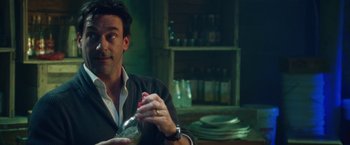 Movie still from “Keeping Up with the Joneses” (2016), directed by Greg Mottola – A man sitting at a table holding a glass; Close Up shot, Over the shoulder angle