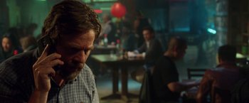 Movie still from “Keeping Up with the Joneses” (2016), directed by Greg Mottola – A man sitting at a table in front of other people in a room; Close Up shot, Over the shoulder angle