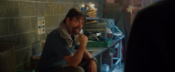 Movie still from “Keeping Up with the Joneses” (2016), directed by Greg Mottola – A man sitting on a bench in front of a table; Medium shot, Over the shoulder angle