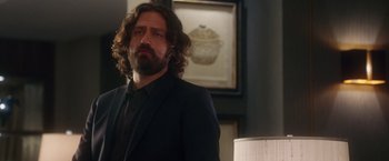 Movie still from “Keeping Up with the Joneses” (2016), directed by Greg Mottola – A man with long hair and a beard standing in a room; Medium shot, Over the shoulder angle