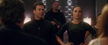 Movie still from “Keeping Up with the Joneses” (2016), directed by Greg Mottola – A man and a woman are holding guns in front of a wall; Medium shot, Over the shoulder angle