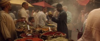 Movie still from “Keeping Up with the Joneses” (2016), directed by Greg Mottola – A group of people standing around a table filled with bowls of food; Medium shot, Over the shoulder angle
