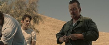 Movie still from “The Last Rampage” (2017), directed by Dwight H. Little – A man smoking a cigarette while standing next to another man in a field; Medium shot, Over the shoulder angle