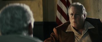 Movie still from “The Last Rampage” (2017), directed by Dwight H. Little – An older man sitting in front of an american flag; Close Up shot, Over the shoulder angle