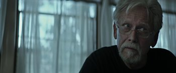 Movie still from “The Last Rampage” (2017), directed by Dwight H. Little – An older man wearing glasses sitting in front of a window; Close Up shot, Over the shoulder angle