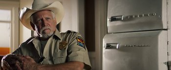 Movie still from “The Last Rampage” (2017), directed by Dwight H. Little – An older man wearing a cowboy hat sitting in front of a refrigerator; Close Up shot, Over the shoulder angle
