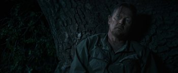 Movie still from “The Last Rampage” (2017), directed by Dwight H. Little – A man sitting next to a tree in a dark room; Close Up shot, Over the shoulder angle