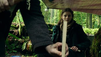 Movie still from “Leave No Trace” (2018), directed by Debra Granik – A person holding a stick in a forest; Medium shot, Over the shoulder angle