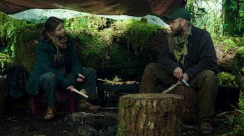 Movie still from “Leave No Trace” (2018), directed by Debra Granik – A man and a woman sitting on a stump; Medium shot, Over the shoulder angle