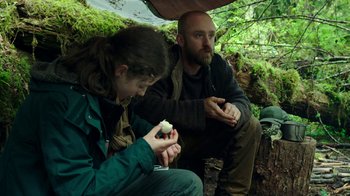 Movie still from “Leave No Trace” (2018), directed by Debra Granik – A man and a woman sitting on the ground; Medium shot, Over the shoulder angle
