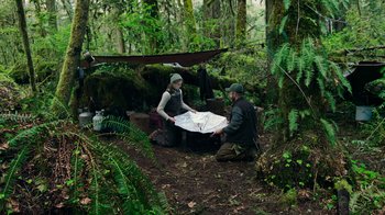 Movie still from “Leave No Trace” (2018), directed by Debra Granik – A man and a woman sitting in the woods with a map; Wide shot, High angle