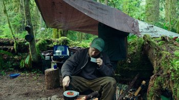 Movie still from “Leave No Trace” (2018), directed by Debra Granik – A man sitting under an awning while eating food; Medium shot, High angle