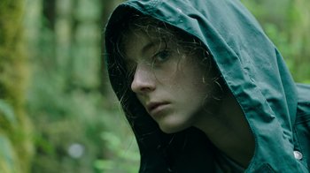 Movie still from “Leave No Trace” (2018), directed by Debra Granik – A young woman wearing a green rain jacket; Close Up shot, Low angle