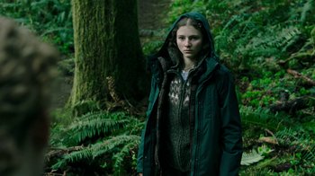 Movie still from “Leave No Trace” (2018), directed by Debra Granik – A young woman in a green jacket standing in the woods; Medium shot, Low angle