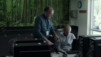 Movie still from “Leave No Trace” (2018), directed by Debra Granik – A man standing next to a man sitting at a computer; Medium shot, Over the shoulder angle