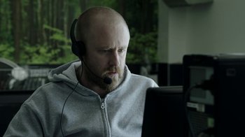 Movie still from “Leave No Trace” (2018), directed by Debra Granik – A man with a beard wearing headphones looking at a computer screen; Close Up shot, High angle