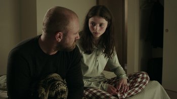 Movie still from “Leave No Trace” (2018), directed by Debra Granik – A man sitting next to a girl on a bed; Medium shot, Over the shoulder angle