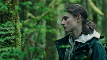 Movie still from “Leave No Trace” (2018), directed by Debra Granik – A young woman in a jacket is standing in the woods; Close Up shot, Over the shoulder angle