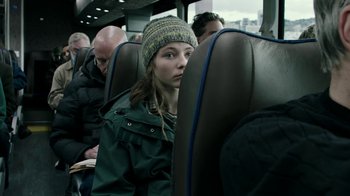Movie still from “Leave No Trace” (2018), directed by Debra Granik – A girl in a green jacket and a hat is sitting on a bus; Close Up shot, Over the shoulder angle