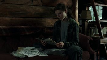 Movie still from “Leave No Trace” (2018), directed by Debra Granik – A woman sitting on a couch looking at papers; Medium shot, High angle