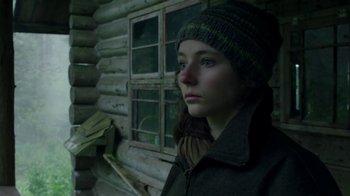 Movie still from “Leave No Trace” (2018), directed by Debra Granik – A woman in a hat and jacket in front of a log cabin; Close Up shot, Low angle