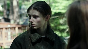 Movie still from “Leave No Trace” (2018), directed by Debra Granik – A young woman with long dark hair wearing a jacket; Close Up shot, Over the shoulder angle