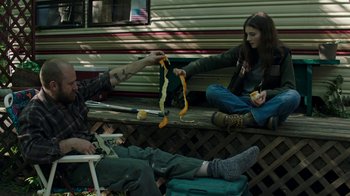 Movie still from “Leave No Trace” (2018), directed by Debra Granik – Two people sitting on a bench and one is holding a ribbon; Medium shot, Low angle