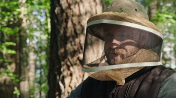 Movie still from “Leave No Trace” (2018), directed by Debra Granik – A man wearing a bee keeper's hat in front of a tree; Close Up shot, Low angle