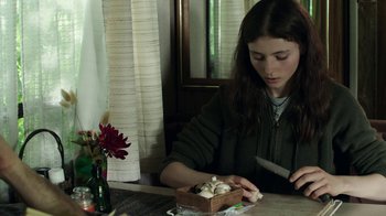 Movie still from “Leave No Trace” (2018), directed by Debra Granik – A woman sitting at a table with a bowl of mushrooms; Medium shot, Over the shoulder angle