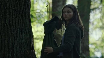 Movie still from “Leave No Trace” (2018), directed by Debra Granik – A woman holding onto a green bag hanging from a tree in the woods; Medium shot, Low angle