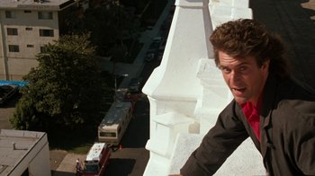 Movie still from “Lethal Weapon” (1987), directed by Richard Donner – A man on the side of a building with a bus in the background; Close Up shot, Low angle