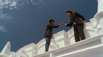Movie still from “Lethal Weapon” (1987), directed by Richard Donner – Two men shaking hands on a white building; Wide shot, Low angle