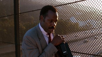 Movie still from “Lethal Weapon” (1987), directed by Richard Donner – A man in a gray suit and red tie holding a black bag; Close Up shot, Low angle